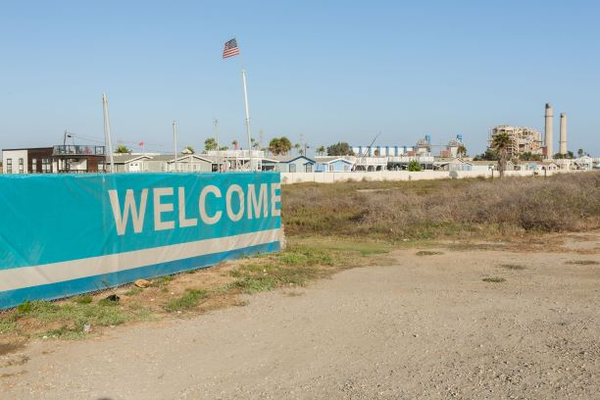 Image of a sign that says "Welcome" on a sandy area with beach houses in the background