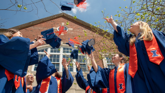 Image of students in graduation regalia tossing their mortar board caps into the air.