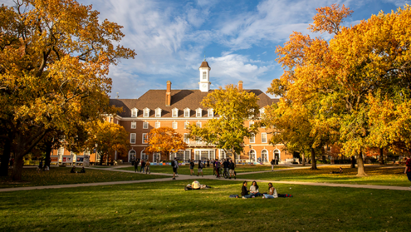 Illinois campus quad in autumn, with a brick building in the background and students on the lawn.