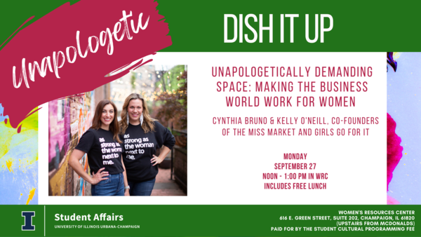 Two women standing in front of a painted brick wall wearing shirts that say "As Strong as the Woman Next to Me"