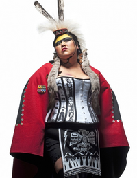 Photograph of Skeena Reece facing the camera, dressed in a combination of contemporary and traditional indigenous clothing.