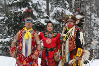 A photograph of two men and one woman in traditional, Native American dress.