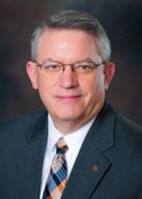 Professor Gregory Harris, wearing glasses, a plaid tie, and a navy blazer