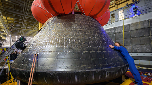NASA astronaut Christina Koch hugs the Orion spacecraft in the well deck of USS John P. Murtha.