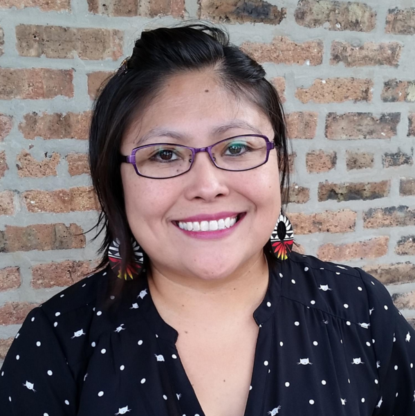 Photo of speaker Yepa-Pappan smiling and looking toward the camera. The artist wears purple prescription glasses and a black and white cat head and polka dot tunic blouse with a low v-cut.