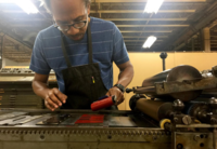 Image of artist, designer, and letterpress printer Ben Blount in his workshop wearing a navy blue shirt with white stripes and a black apron.