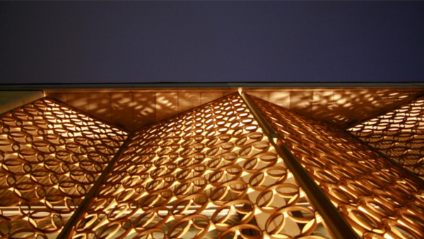 Gold decorative screens similar to folding closet doors are being shown from below. Light is emanating from the inside casting sun-like speckles about the roof of the panels.