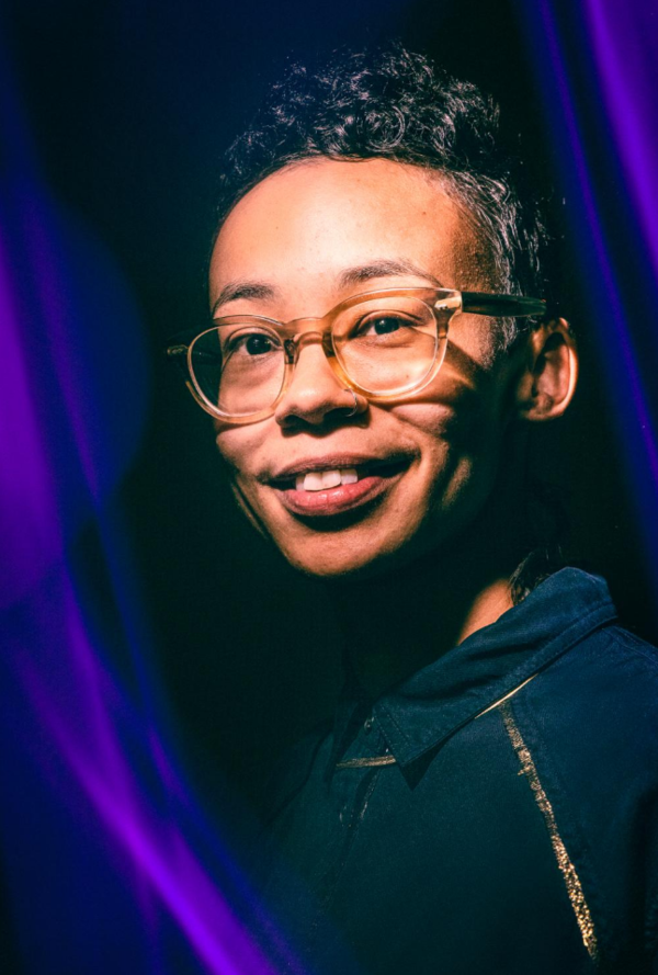 Passionate adult woman with a toothy smile and wearing translucent prescription glasses. There are streaks of violet to her left and upper right.