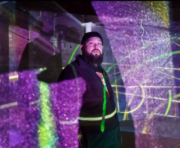 Adult male artist in the middle of purple and green projected lights