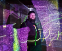 Adult male artist in the middle of purple and green projected lights