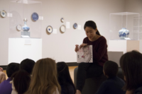 Adult woman presenting a picture book to young children sitting in front of her