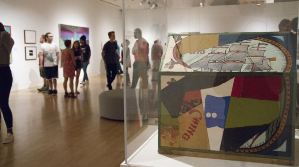 Diverse set of visitors in a museum exhibit admiring paintings and objects on display behind glass coverings.
