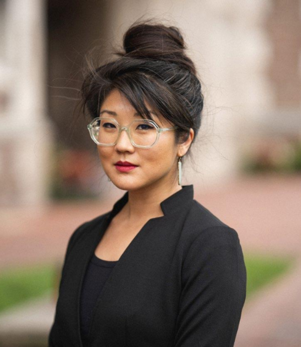 Adult woman wearing all black looking ahead. The background is blurred.