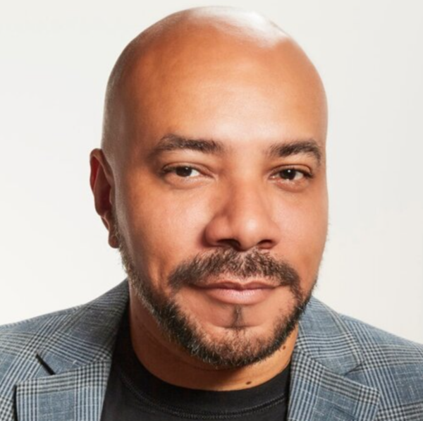 adult man charismatically smiling into the camera wearing a plaid blazer