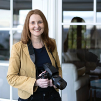 Adult woman resting her black camera with both of her hands and smiling a toothy smile