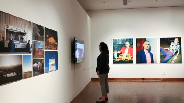 Room full of photographs with a television on a wall to the left. Woman watches the television intently