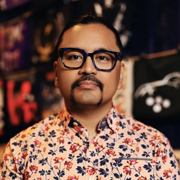Headshot of grown man look forward wearing glasses and a floral button-up peach shirt