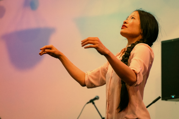 Side photo of a woman looking expressively up at the sky with her hands conductor-like in front of her.