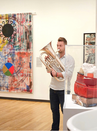 college student playing tube near artwork in gallery