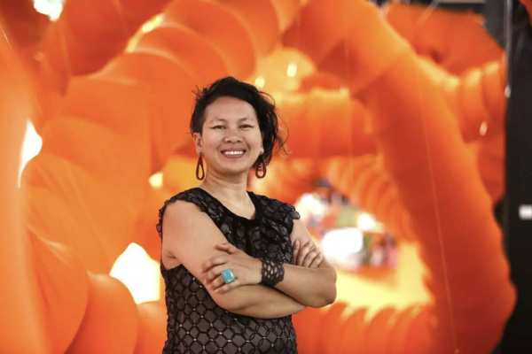 Anida Yoeu Ali standing in front of huge orange coils, smiling