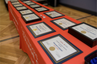 On an orange table cloth, sits in two rows, award certificates for recipients of the 2025 Student Awards.