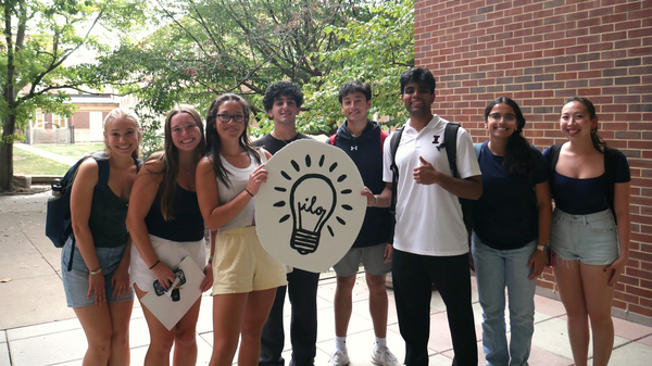 A group of students holds a large poster showing a light bulb and "ILO"