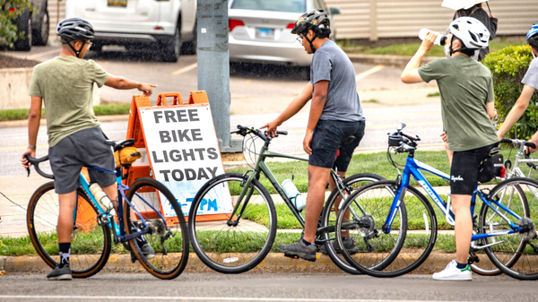 Three people with helmets on bicyles next to a "Free Bike Light" sign