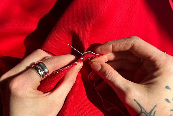 an image of hands stitching rips into a red cloth