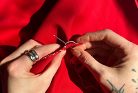 an image of hands stitching rips into a red cloth