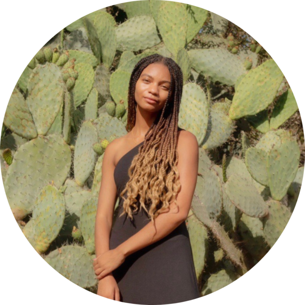 Photo of Leah Thomas with her hands clasped in front of a large cactus