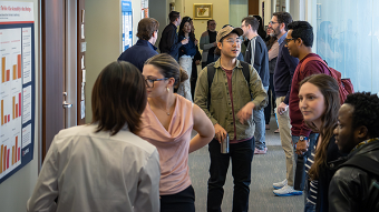 students and faculty interacting in a hallway lined with research posters