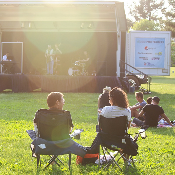 In the forefront a man and woman are having a conversation while a band plays on a stage in the background.