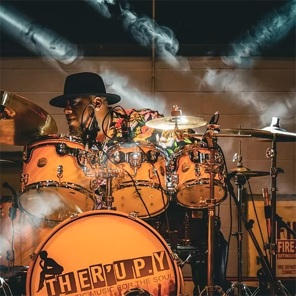A-train of Ther'Up.Y performing on the drums with stage lights and fog in the foreground.