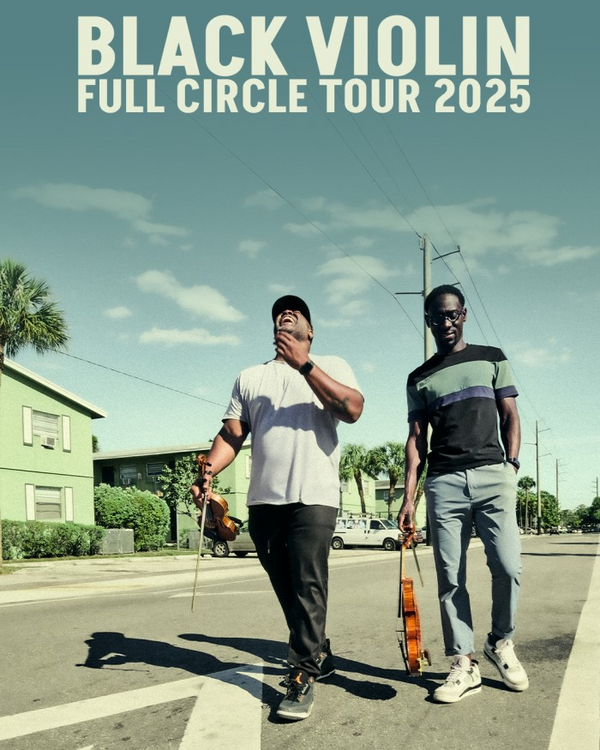 Black Violin Full Circle Tour 2025; Image of Wil Baptiste and Kev Marcus carrying violins while walking down a street in a residential neighborhood.