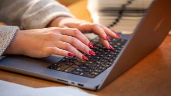 Manicured hands typing on a laptop.