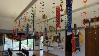 Colorful carp streamers and origami cranes hang from the ceiling in a bright indoor space, creating a festive and culturally inspired display.