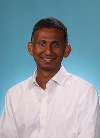 Photo of man with short black hair, wearing a white long-sleeve shirt