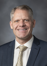 Image of Dr. Grant Jensen. He is smiling and wearing a blue suit with a blue/gold pattern tie.
