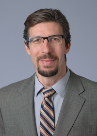 Picture of Dr. Samy Meroueh in suit and tie. He has dark hair and a trimmed circle beard, wearing glasses. He is smiling.