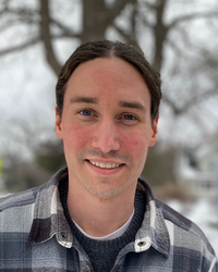 Photo of Prof. David Hershey. He has black hair, parted down the center and is smiling. He is wearing a black and white plaid shirt.