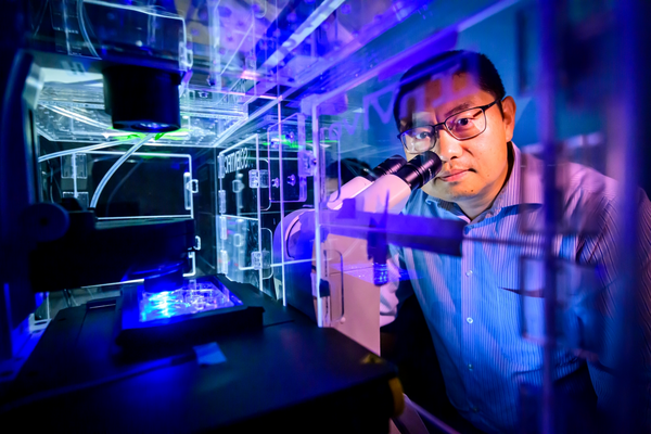 Dr. Kai Zhang - Person with short dark hair and glasses standing behind microscope with other illuminations.