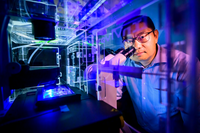 Dr. Kai Zhang - Person with short dark hair and glasses standing behind microscope with other illuminations.